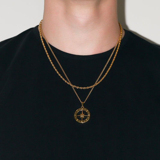 Gold compass pendant necklace set with three chains on dark shirt