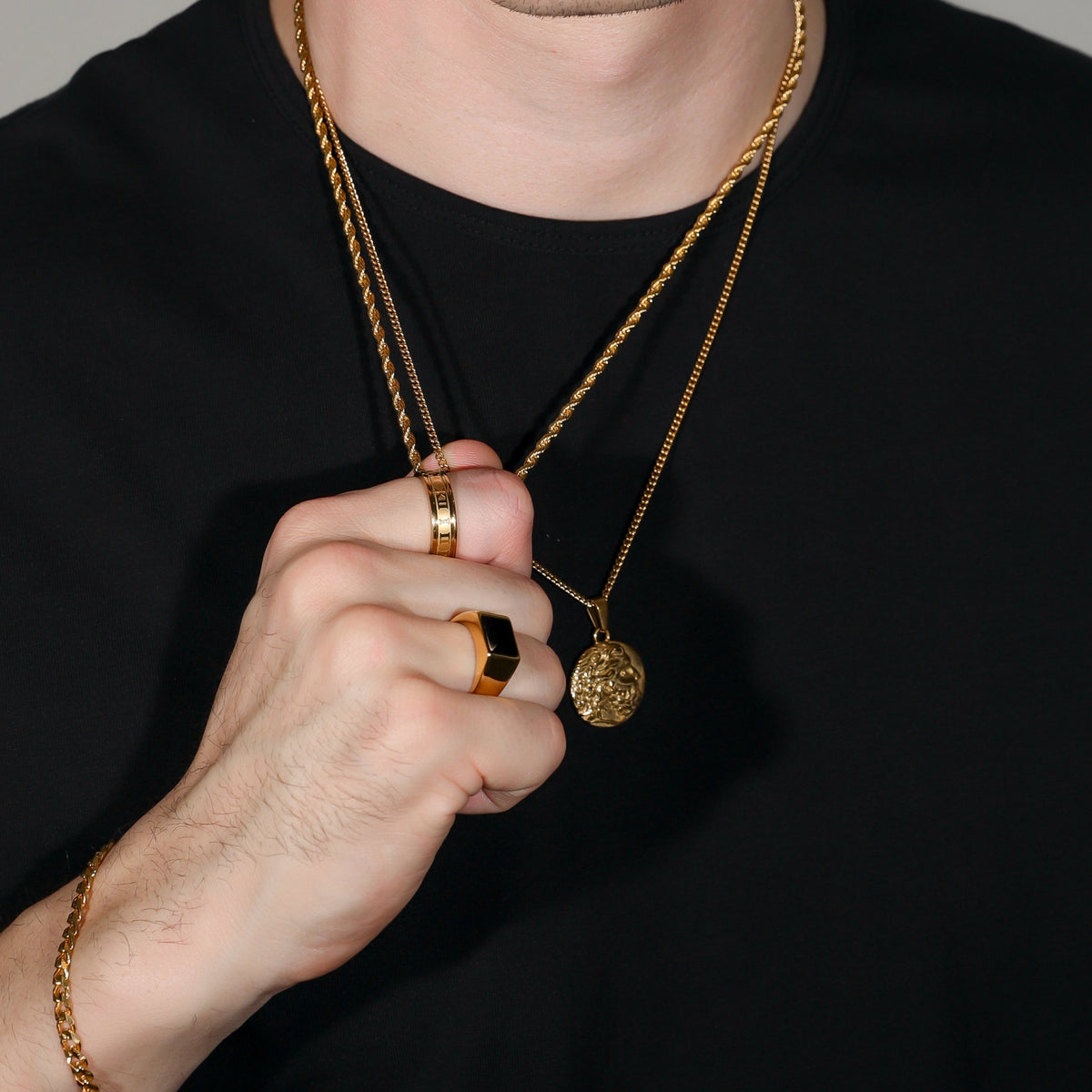 Square black signet ring with gold-toned band, worn with layered necklace