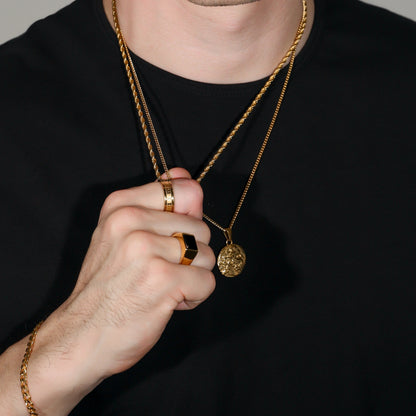 Square black signet ring with gold-toned band, worn with layered necklace