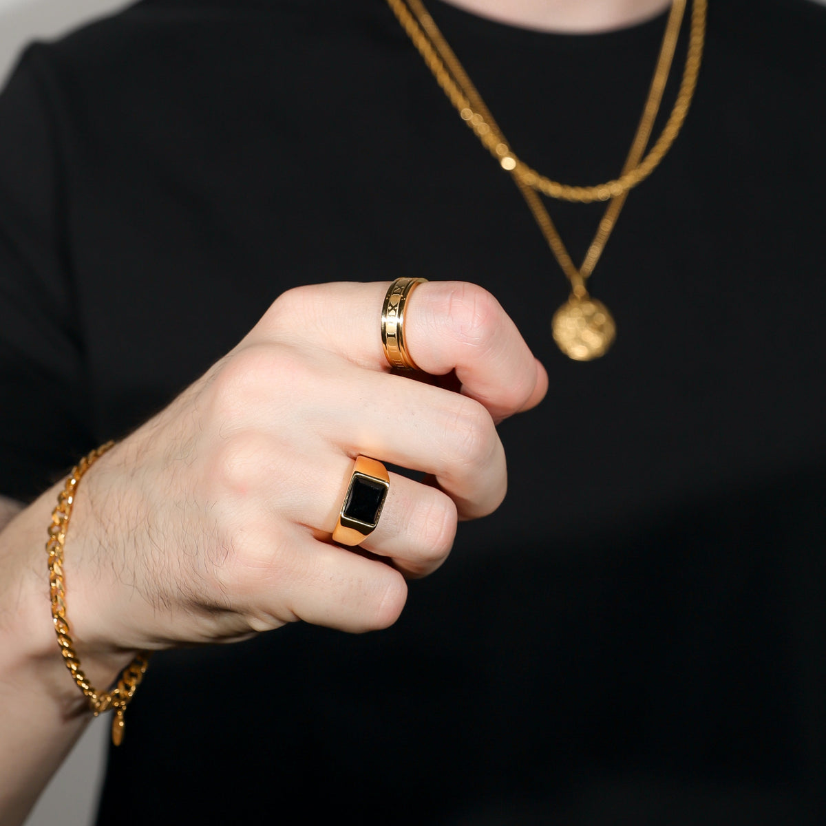 Gold PVD square black signet ring on finger, close-up view