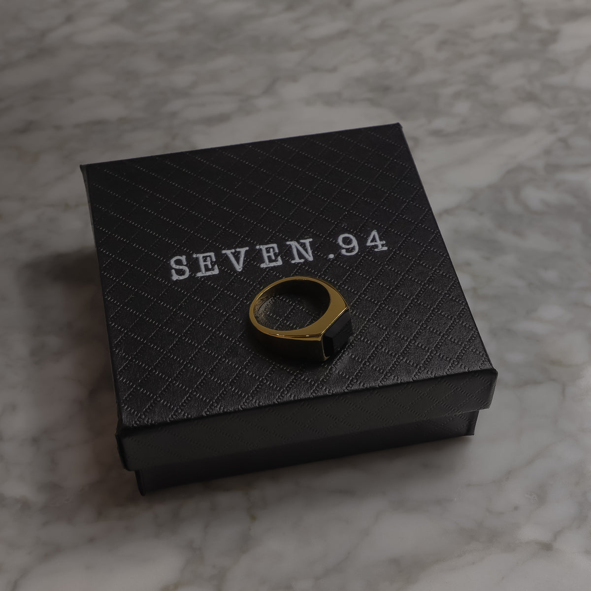 Square black signet ring resting on black gift box