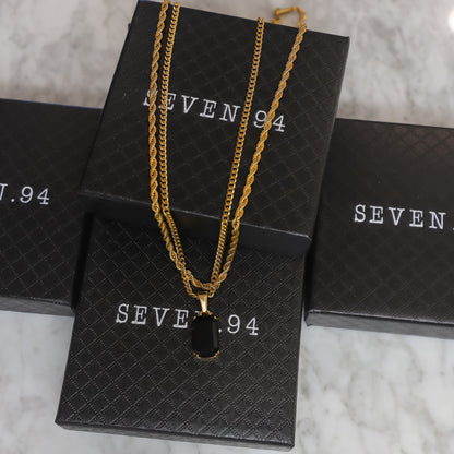 Gold-tone onyx pendant necklace set with dark stone charm on gift bag