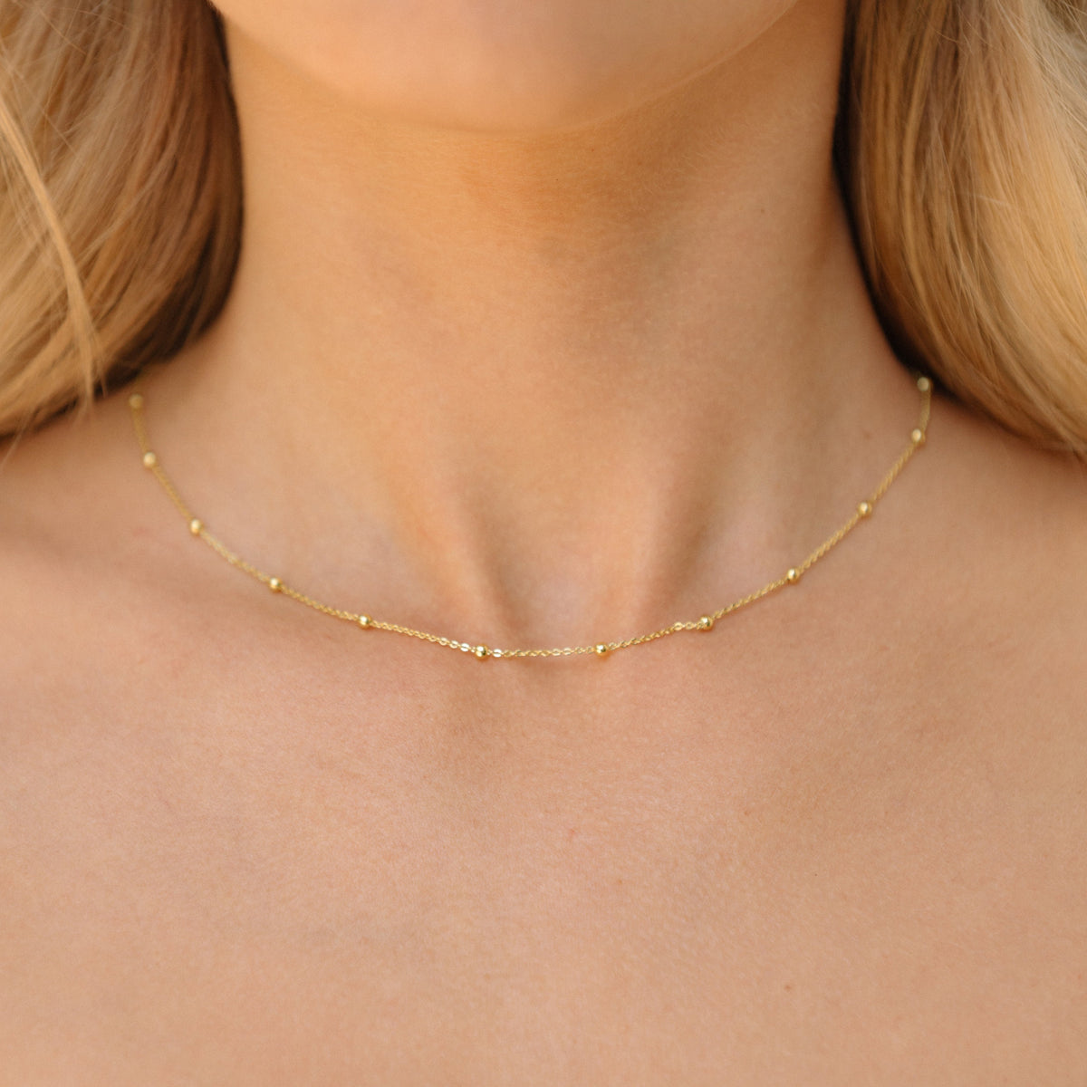 Gold satellite chain necklace with tiny bead stations, worn at the neckline