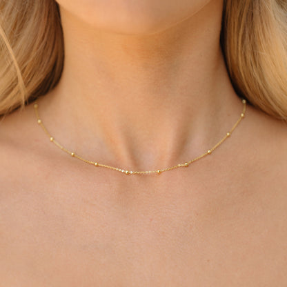 Gold satellite chain necklace with tiny bead stations, worn at the neckline