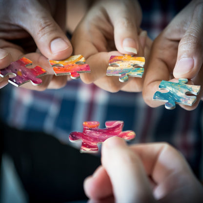 Hands holding small colorful jigsaw puzzle pieces for a unicorn-themed puzzle