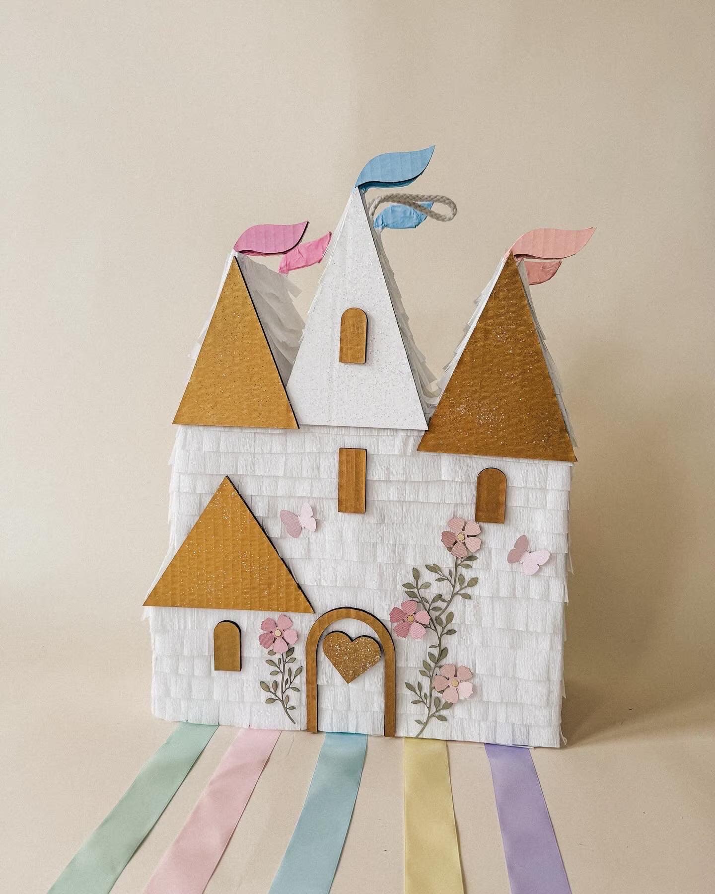 Handmade castle piñata with white stone walls, gold roofs, pastel flags, heart door