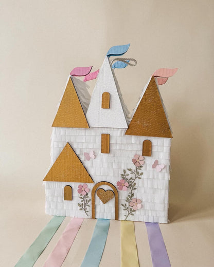 Handmade castle piñata with white stone walls, gold roofs, pastel flags, heart door