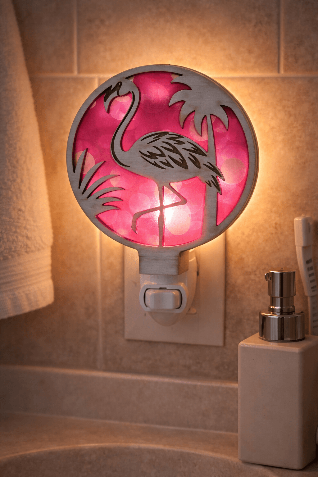 Flamingo LED nightlight with round tropical panel, pink glow lit in wall outlet