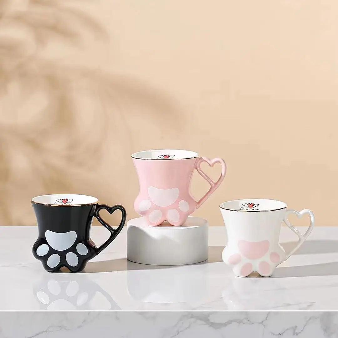 Set of cat paw mugs in black, pink, and white with heart handles and paw pad designs