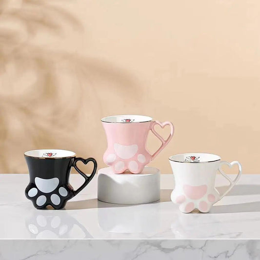 Set of cat paw mugs in black, pink, and white with heart handles and paw pad designs