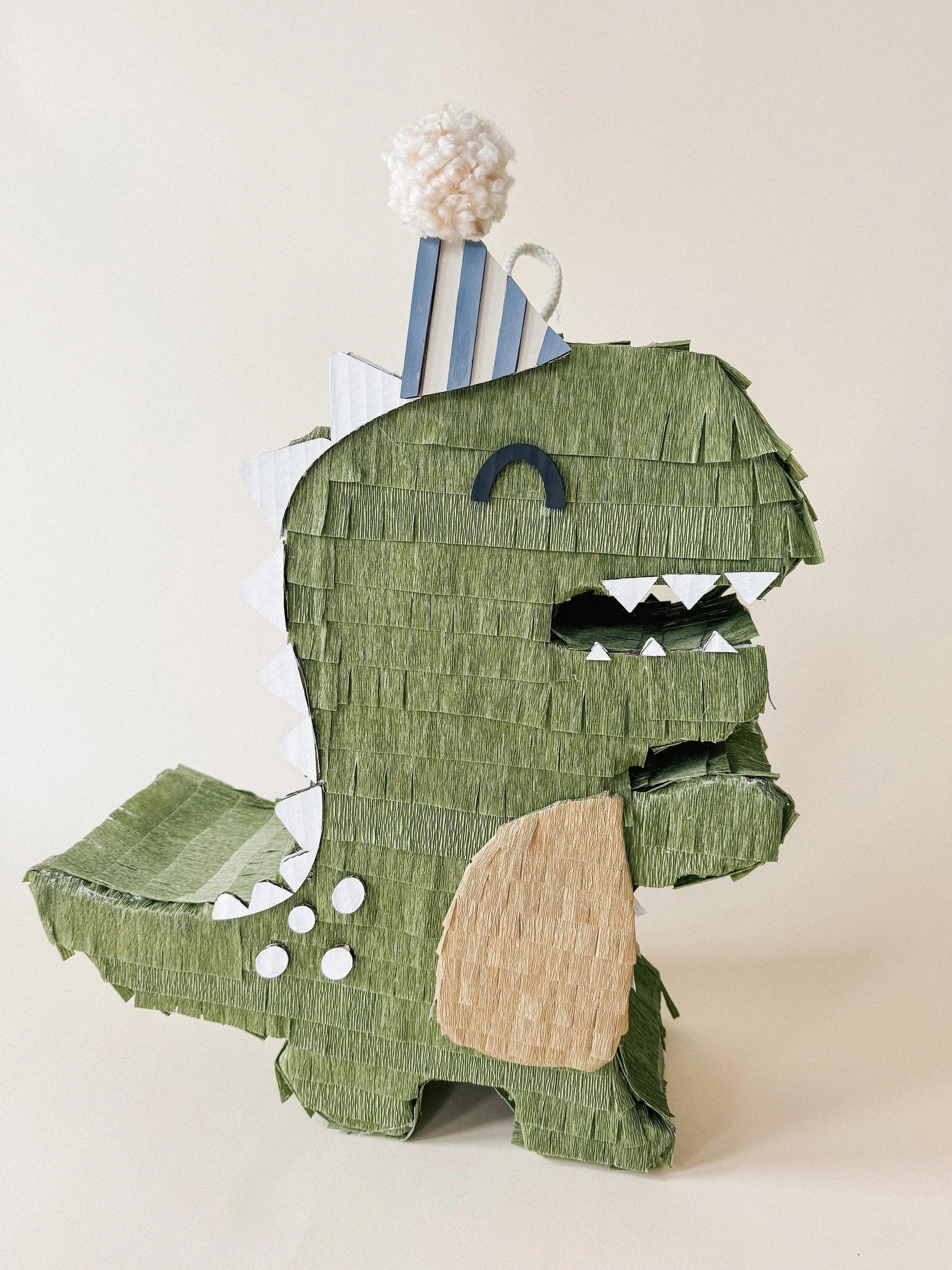 Green dinosaur piñata with blue striped back, beige belly patch and white teeth
