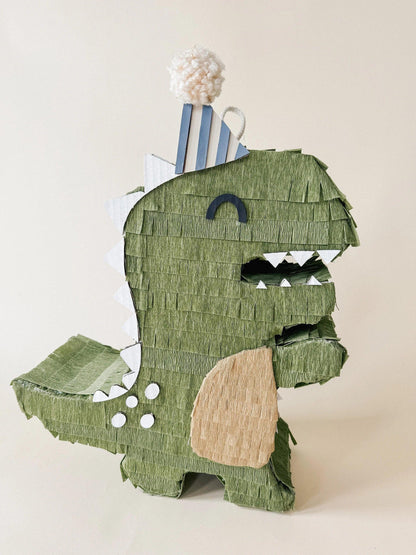 Green dinosaur piñata with blue striped back, beige belly patch and white teeth