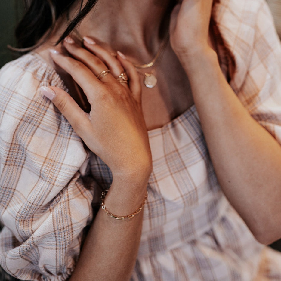 Gold-filled paperclip bracelet worn with layered gold necklaces and rings.