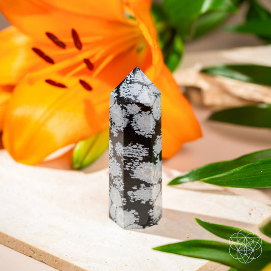 Black and white speckled snowflake obsidian crystal point on light surface