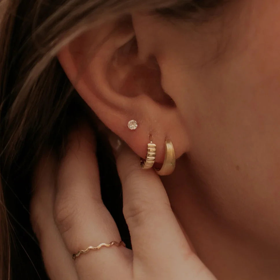 Gold ridged huggie hoop worn beside a plain gold hoop