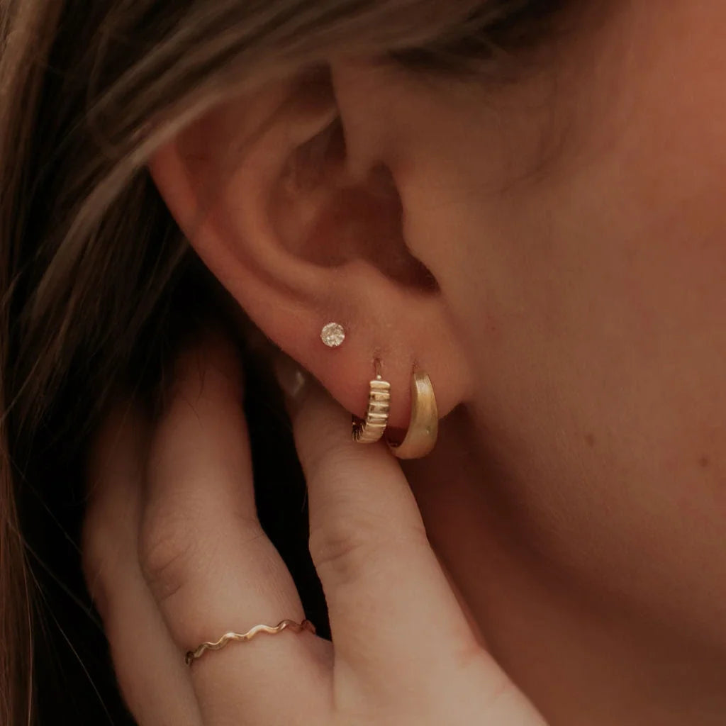 Gold chunky brushed huggie hoop worn alongside a ribbed hoop and stud.