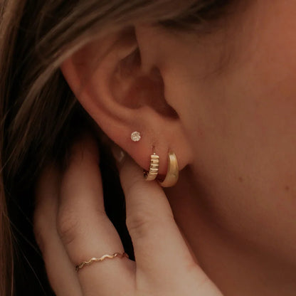 Gold chunky brushed huggie hoop worn alongside a ribbed hoop and stud.