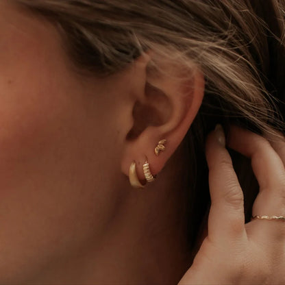 Gold ridged huggie hoop worn beside a plain gold hoop
