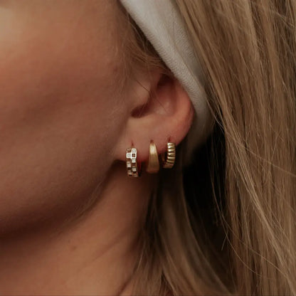 Gold chunky brushed huggie hoop worn with two other small gold hoops.