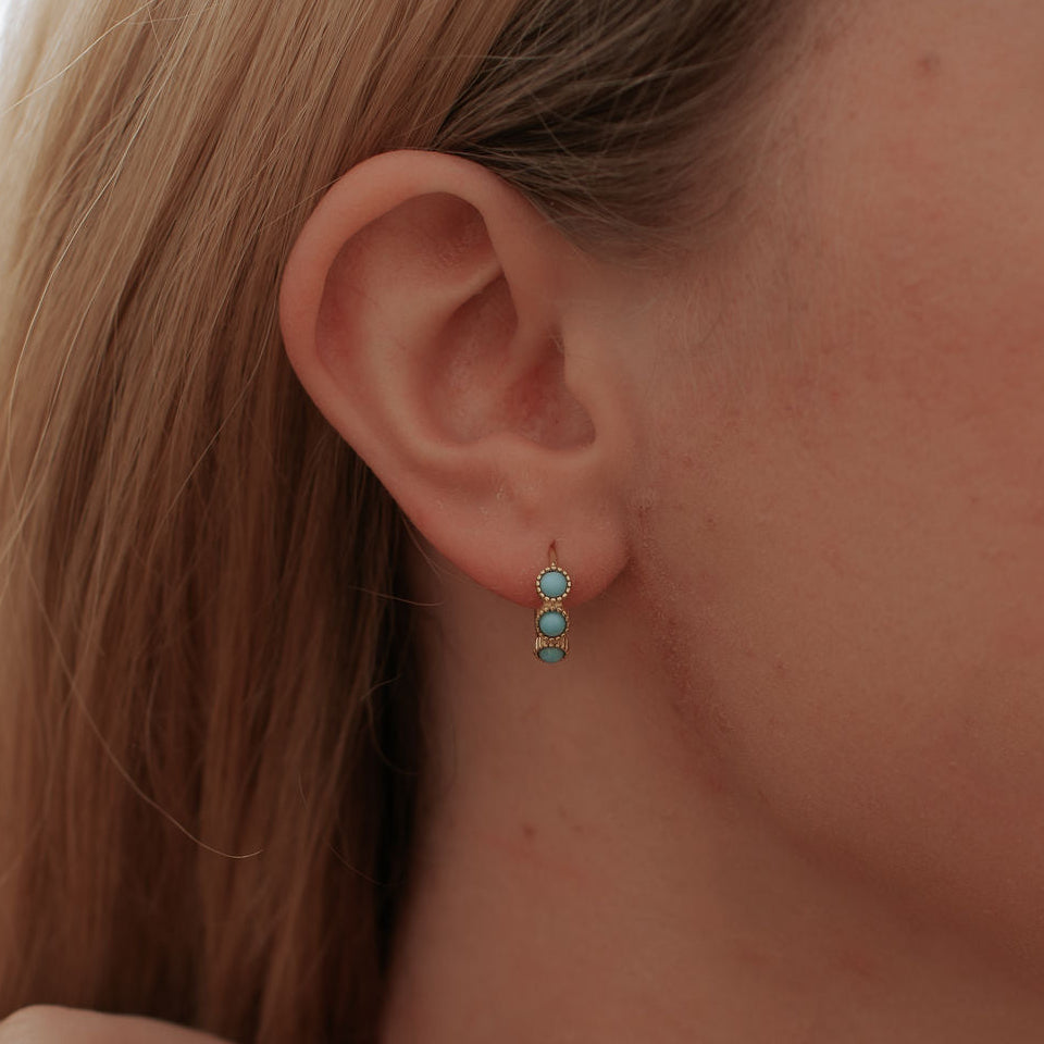 Gold turquoise huggie hoop earring worn on an ear, shown close up.