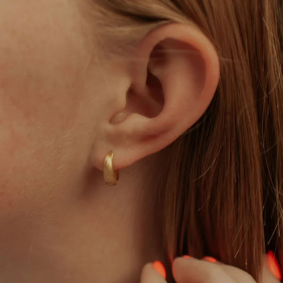 Single gold chunky brushed huggie hoop worn on an earlobe.