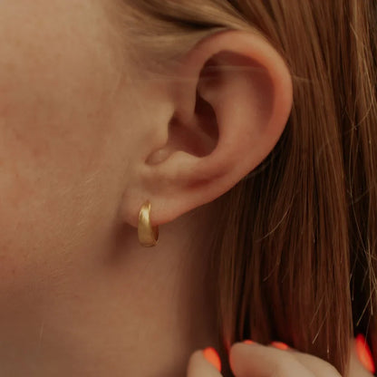 Single gold chunky brushed huggie hoop worn on an earlobe.