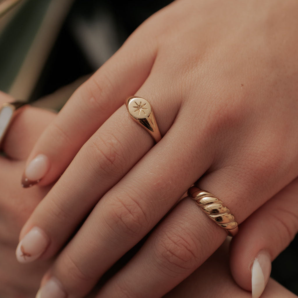 Gold twist ring worn on a hand, showing its raised diagonal ridges