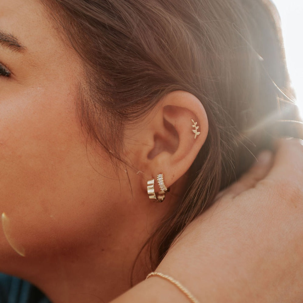Gold Tate hoop earrings with ridged bands, worn alongside other earrings.