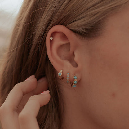 Gold turquoise huggie hoop earrings worn with other small earrings.