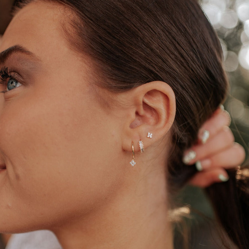 Gold hoop with a small dangling flower charm, worn with other stud and drop earrings