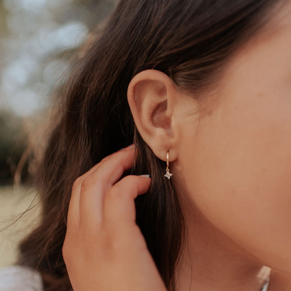 Gold hoop earring with a small sparkling flower charm, worn on the ear