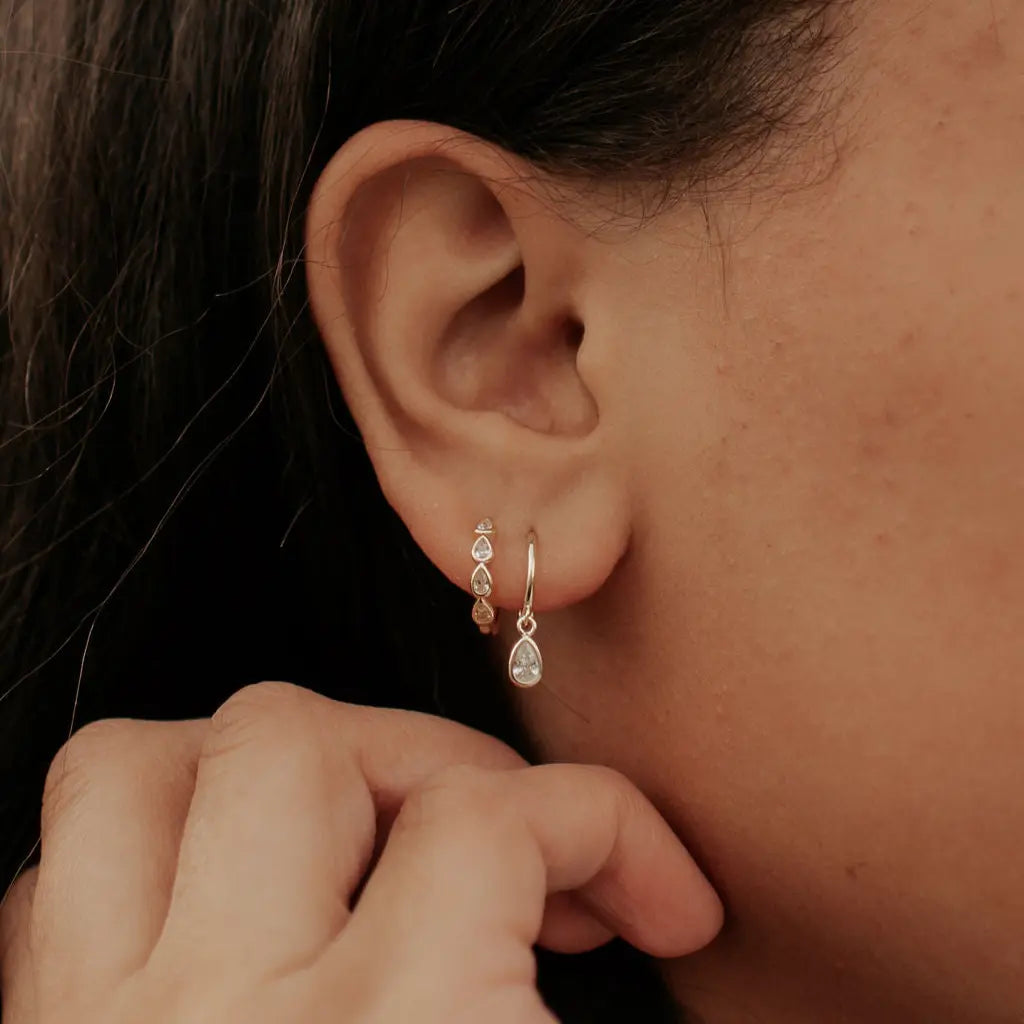 Gold teardrop stone hoop earrings shown worn on an ear.