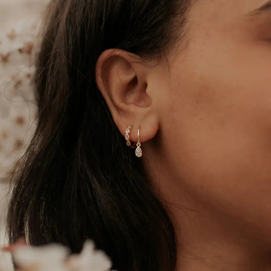 Gold teardrop dangle hoop earrings worn on an ear.