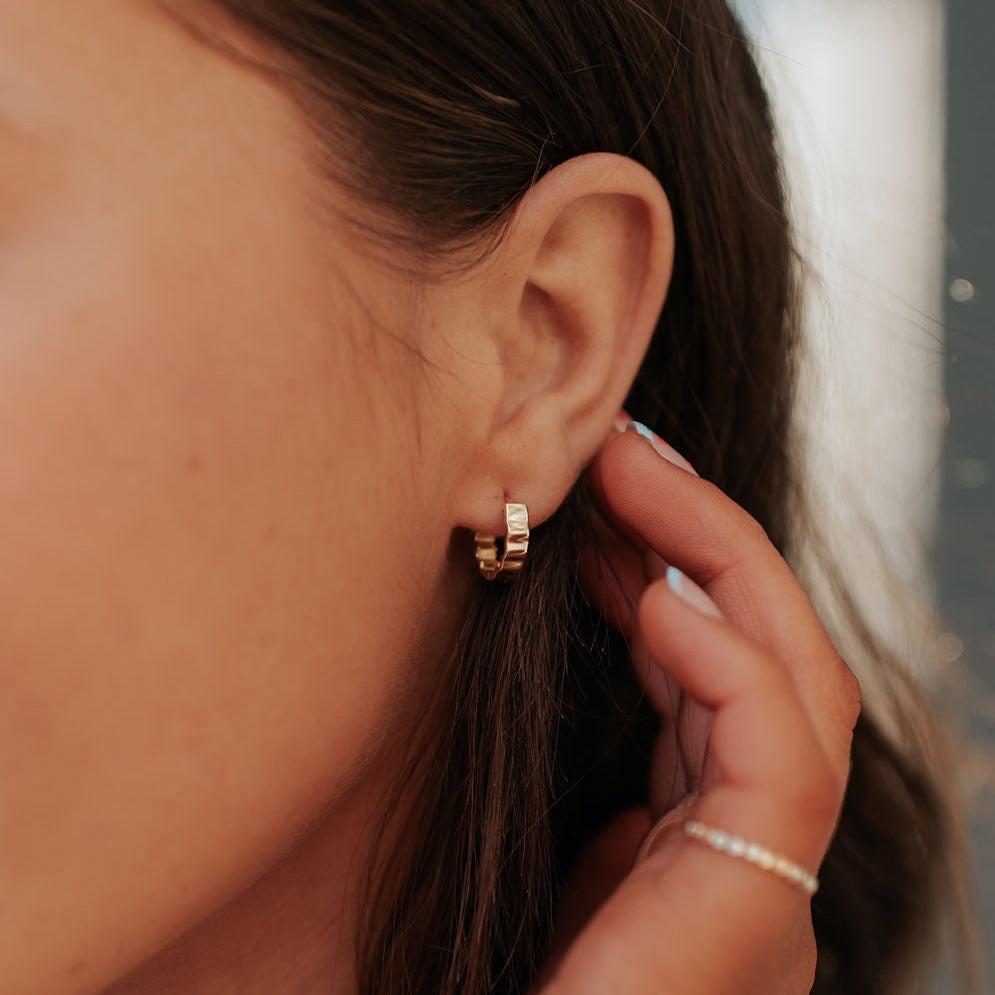 Gold Tate hoop earrings with ridged bands, worn on an ear.