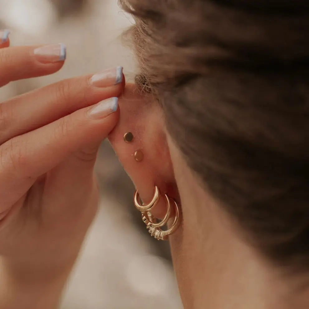 Gold flat back stud worn above layered hoop earrings.