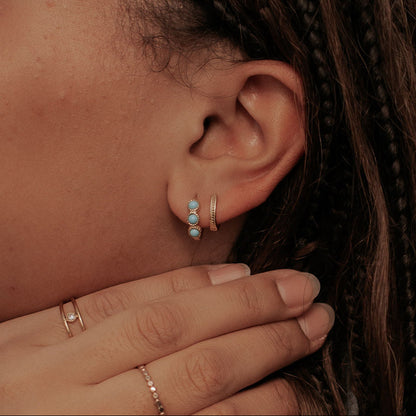 Gold turquoise huggie hoop earrings worn on an ear, shown from the side.