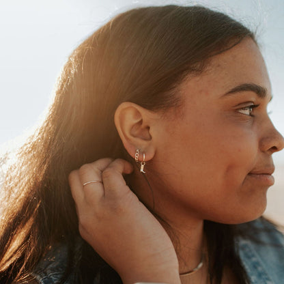 Gold Peri hoops worn on an ear, with a small dangling charm.
