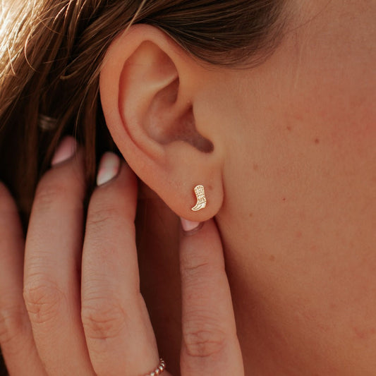 Gold-tone textured boot stud earring worn on the earlobe