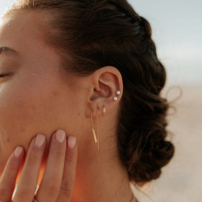 Gold-tone opal stud earrings worn in an ear piercing