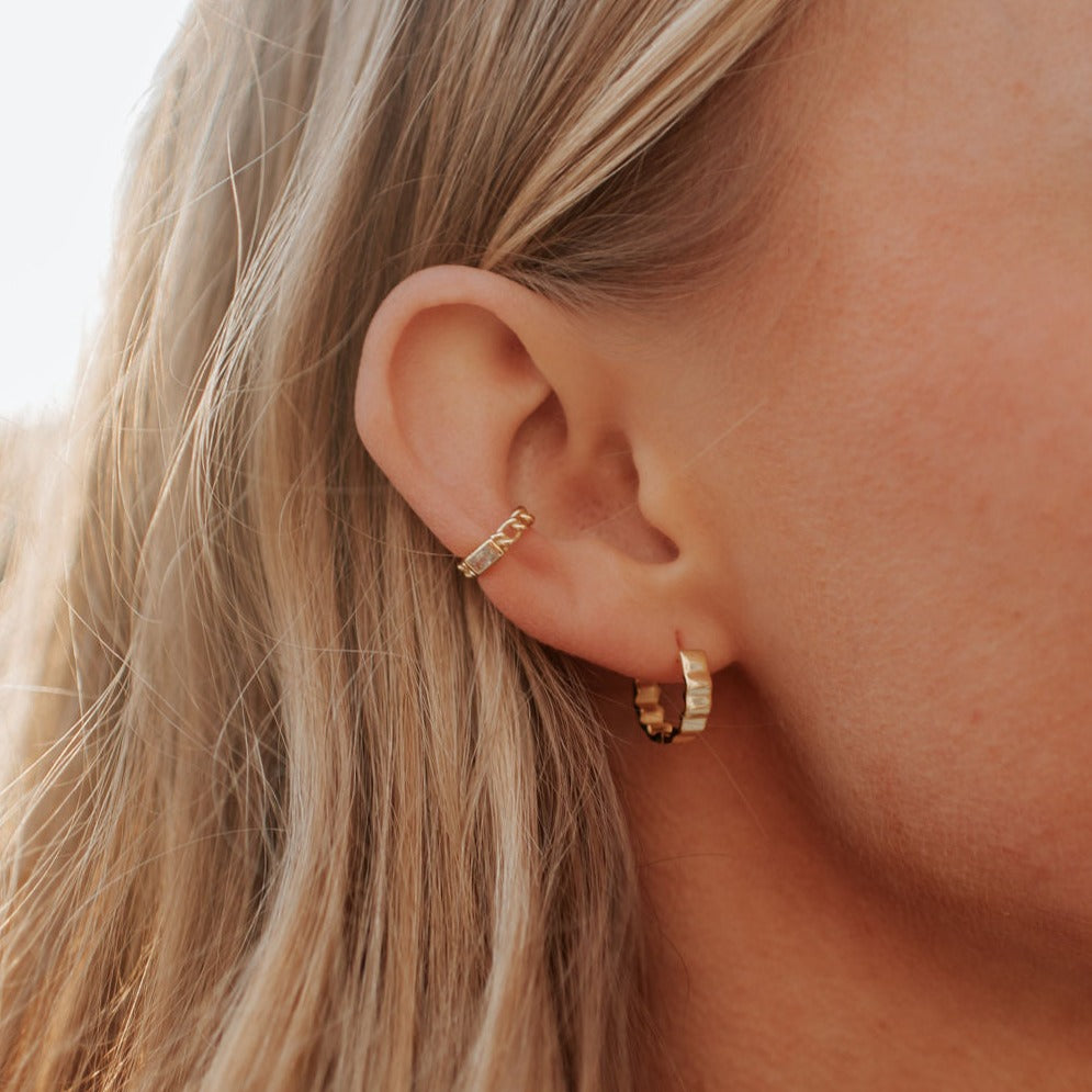 Gold Tate hoop earrings with ridged bands, shown worn on an ear.