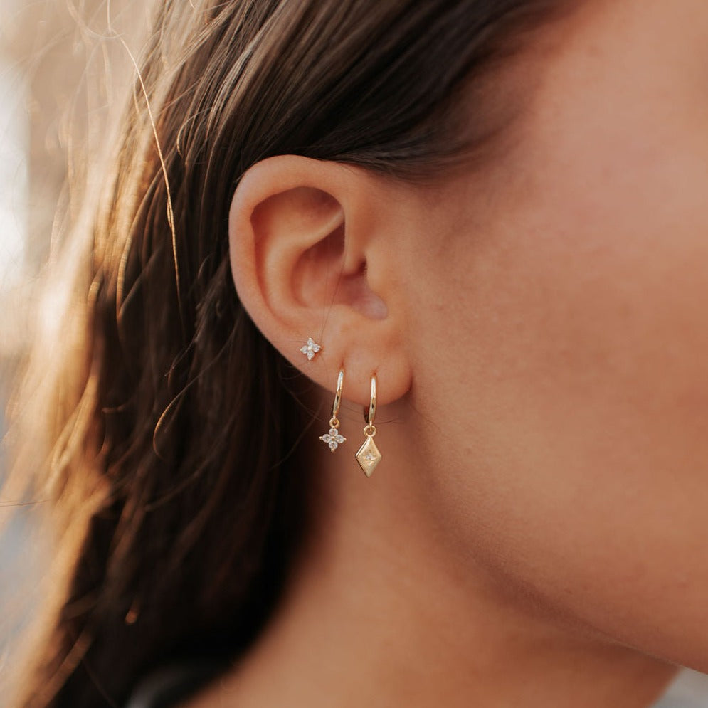 Gold hoop with a dangling flower charm, worn among other earrings