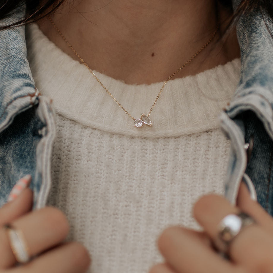 Gold two-stone necklace with clear gems, worn over a sweater