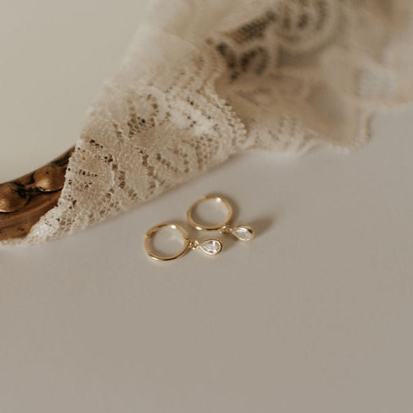 Gold hoop earrings with clear teardrop stones, shown from above.