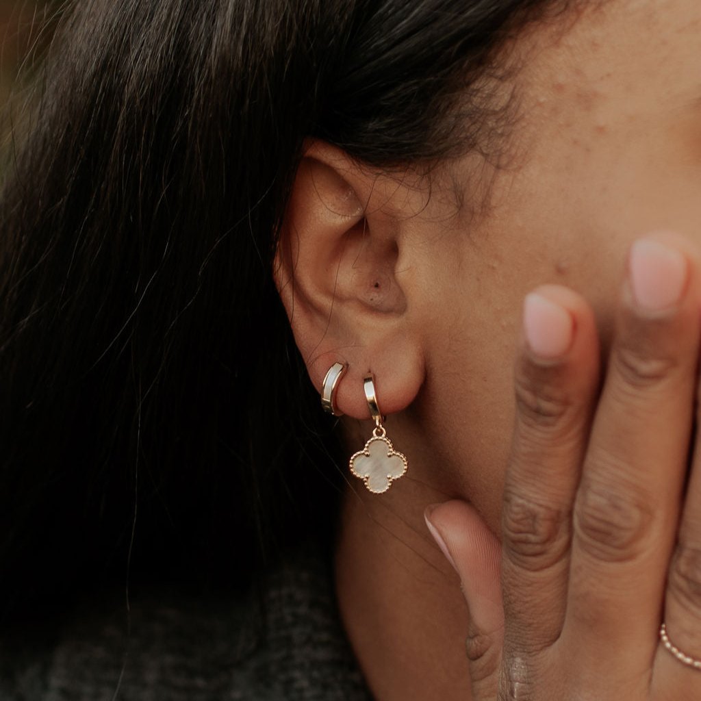 Gold huggie hoops with mother-of-pearl inlay, worn beside a clover charm earring