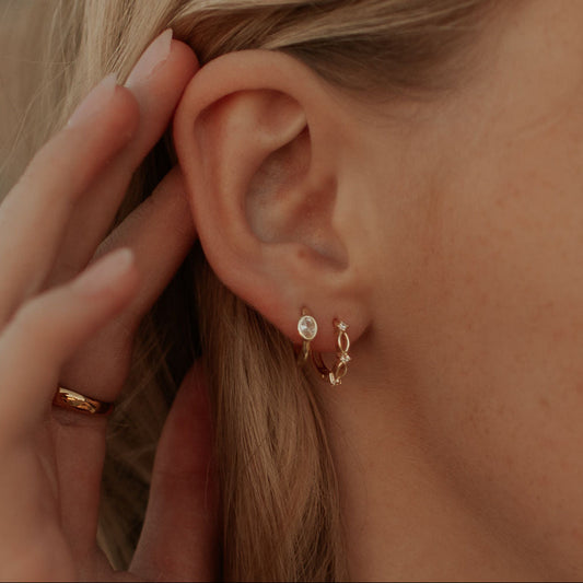 Gold lace huggie hoop earring worn on the earlobe, with delicate openwork details