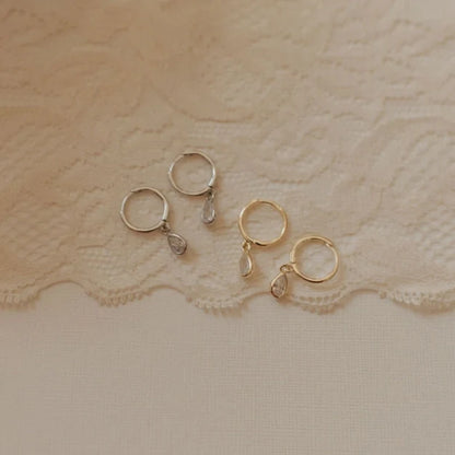 Gold and silver hoop earrings with dangling teardrop stones.