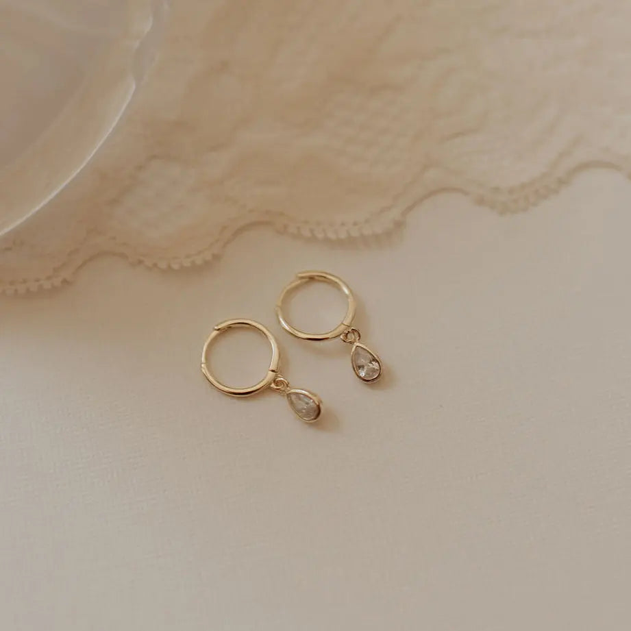 Gold hoop earrings with dangling teardrop cubic zirconia stones.
