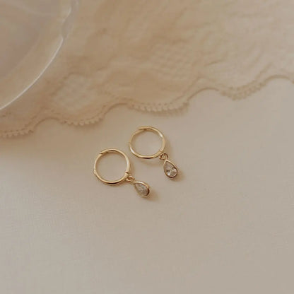 Gold hoop earrings with dangling teardrop cubic zirconia stones.
