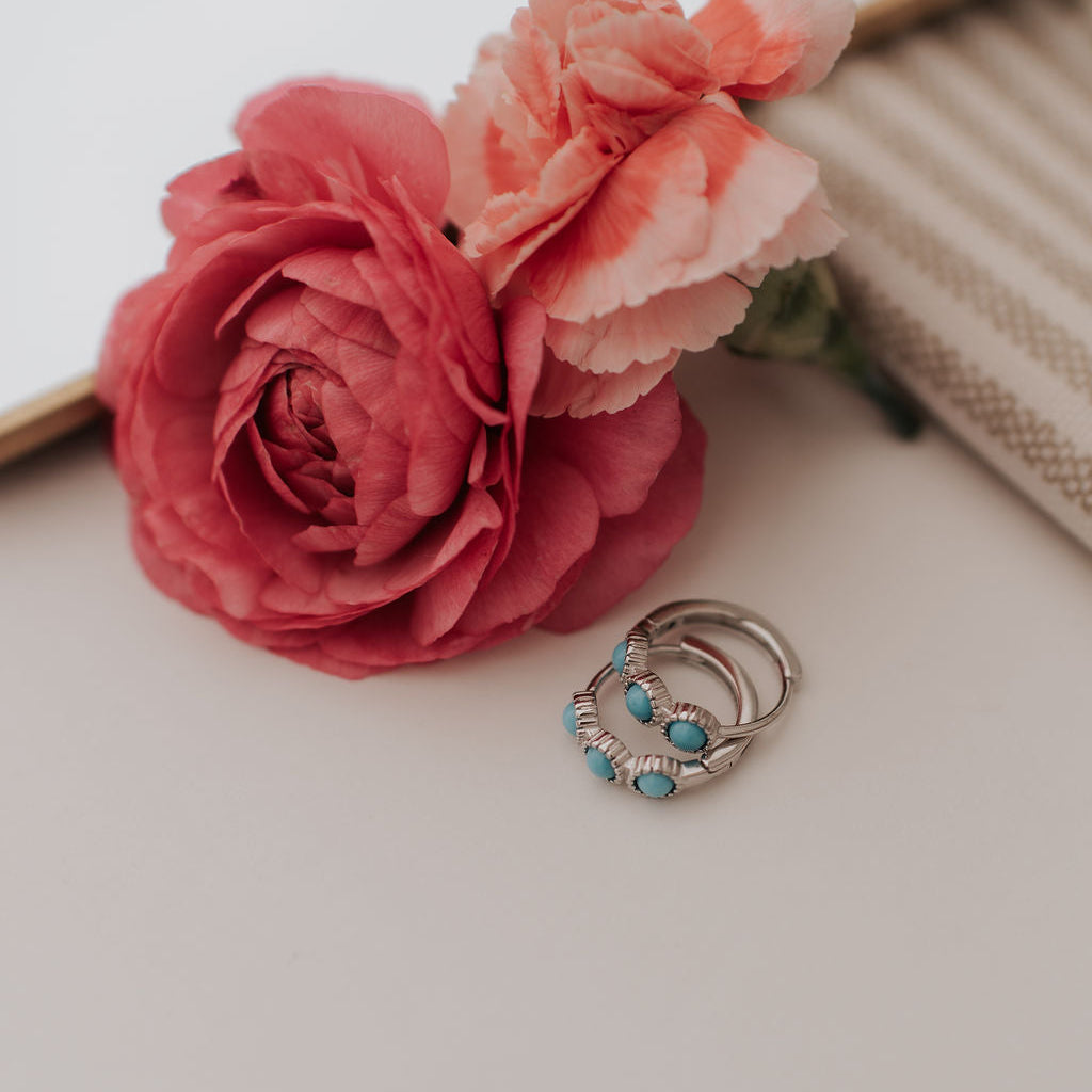 Silver huggie hoop earrings with turquoise stones and ridged detailing.