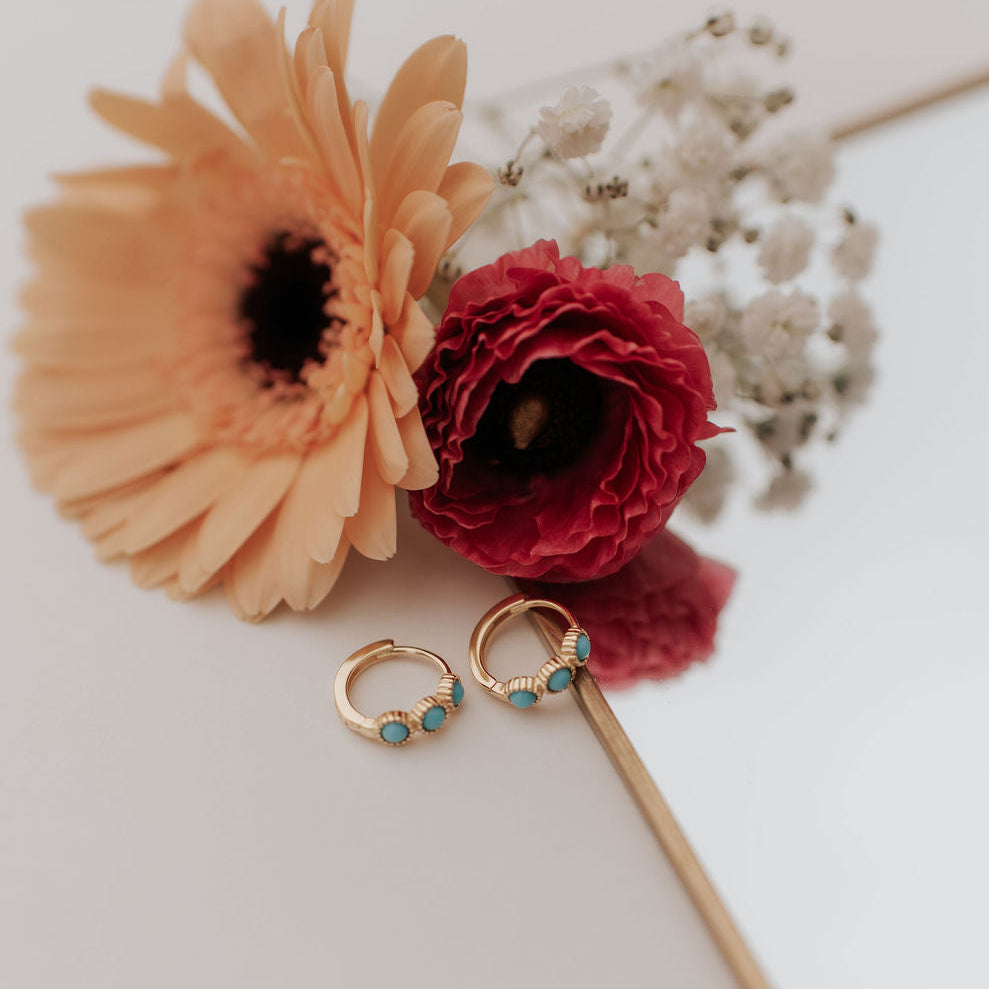 Gold huggie hoops with turquoise stones, shown open to reveal their clasp.